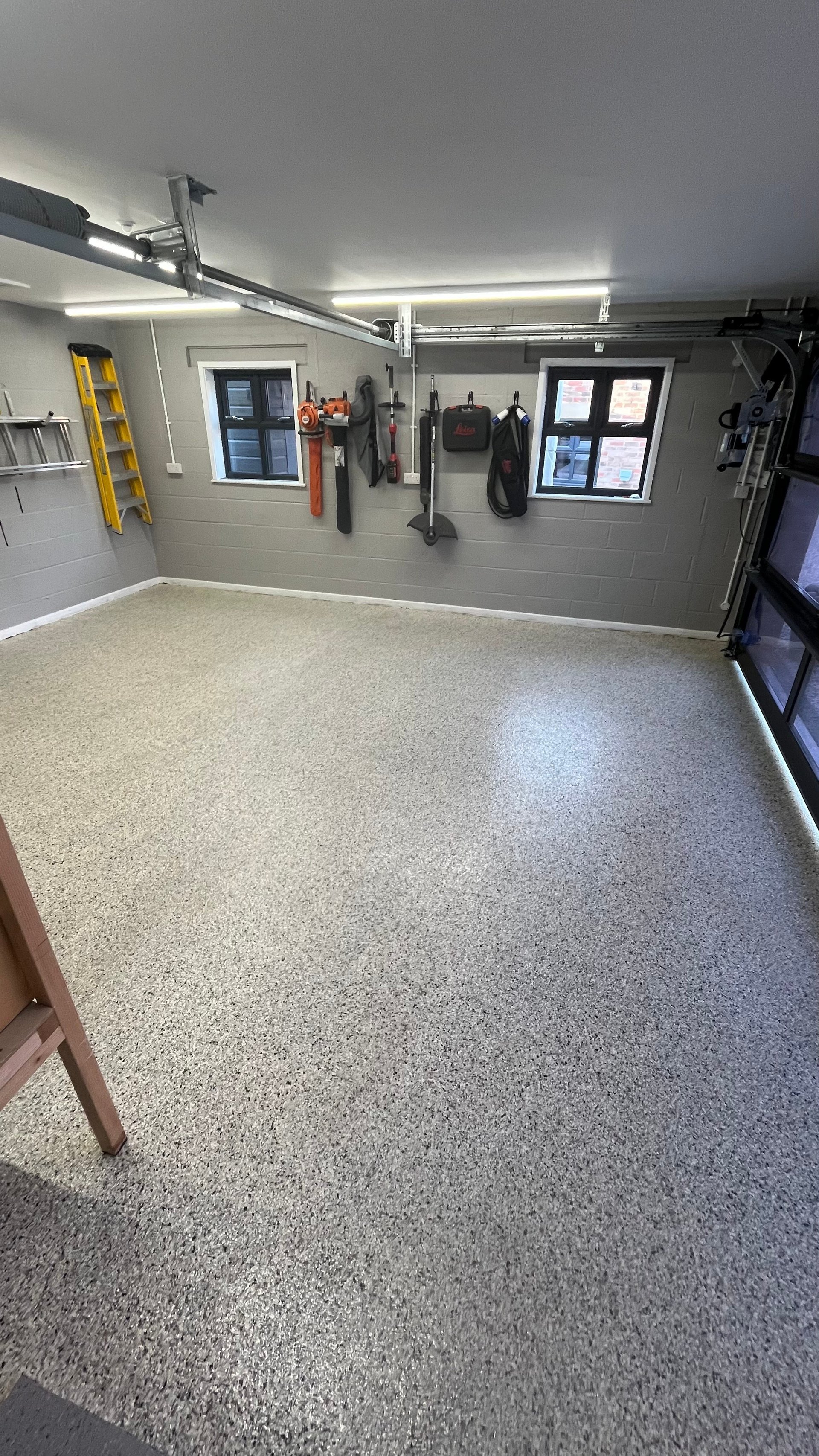 Organized garage interior with epoxy flooring, wall-mounted tools, bright LED lighting, and windows