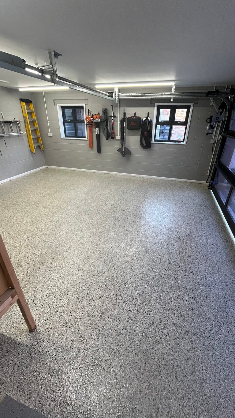 Organized garage interior with epoxy flooring, wall-mounted tools, bright LED lighting, and windows