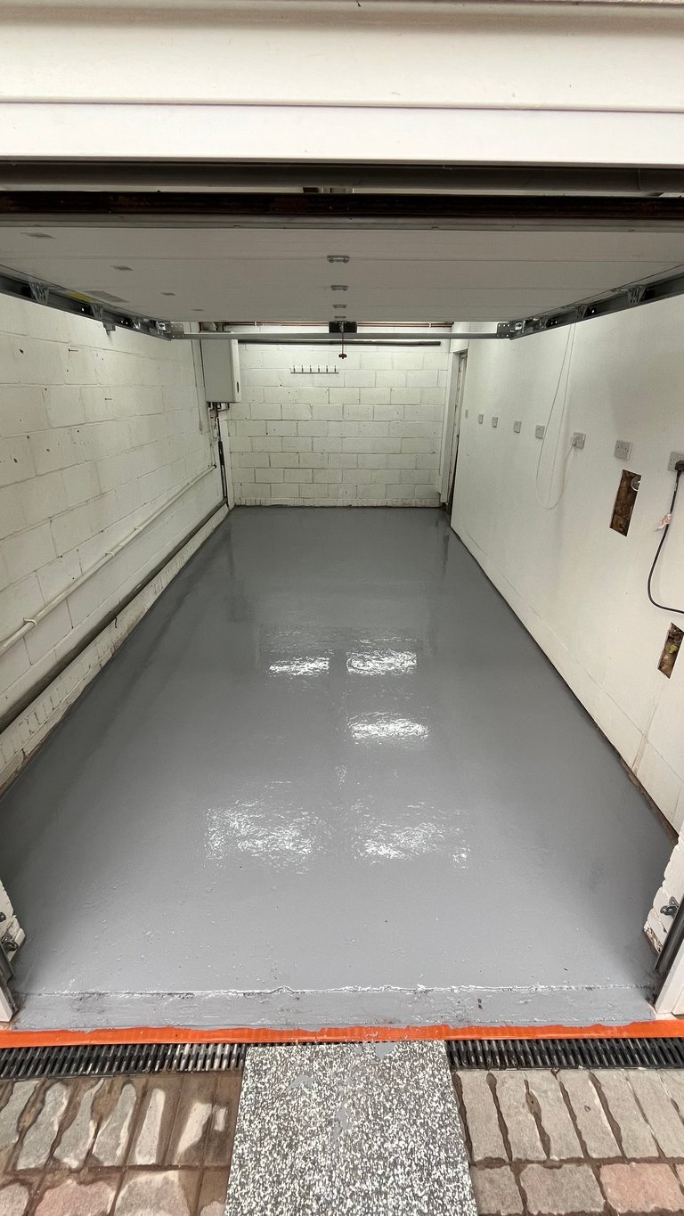 Empty garage interior with gray epoxy floor, white brick walls, and open garage door leading to driveway