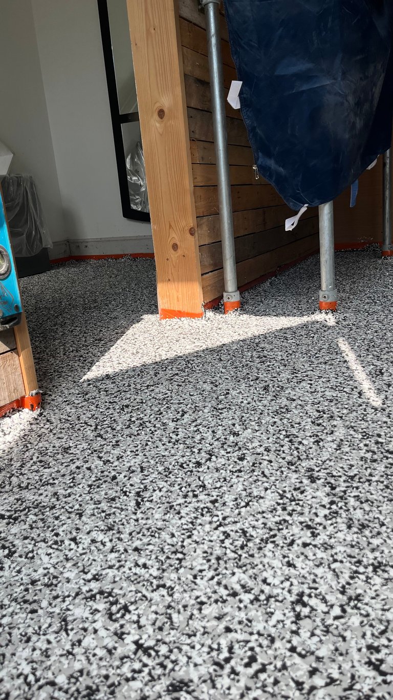 Wooden support beam with metal post on speckled gray garage floor, orange pads at base