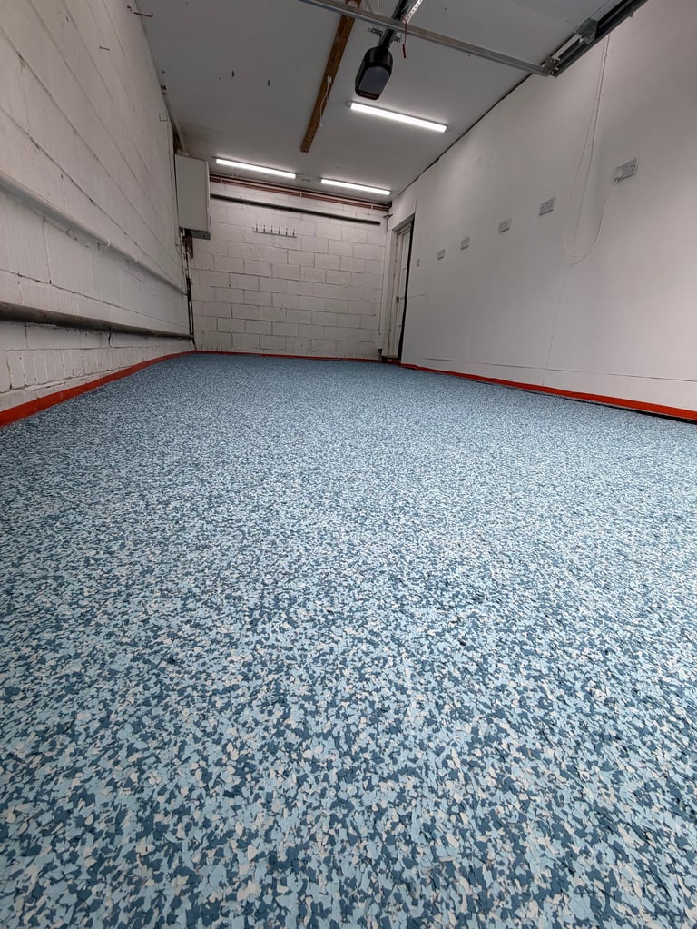 Empty garage interior with blue speckled epoxy floor, white walls, red trim, and overhead lighting