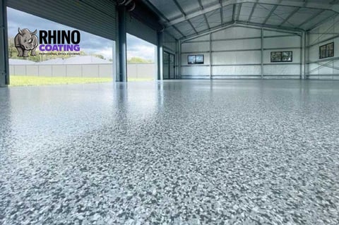Spacious industrial garage with polished concrete epoxy floor and Rhino Coating logo on exterior wall.