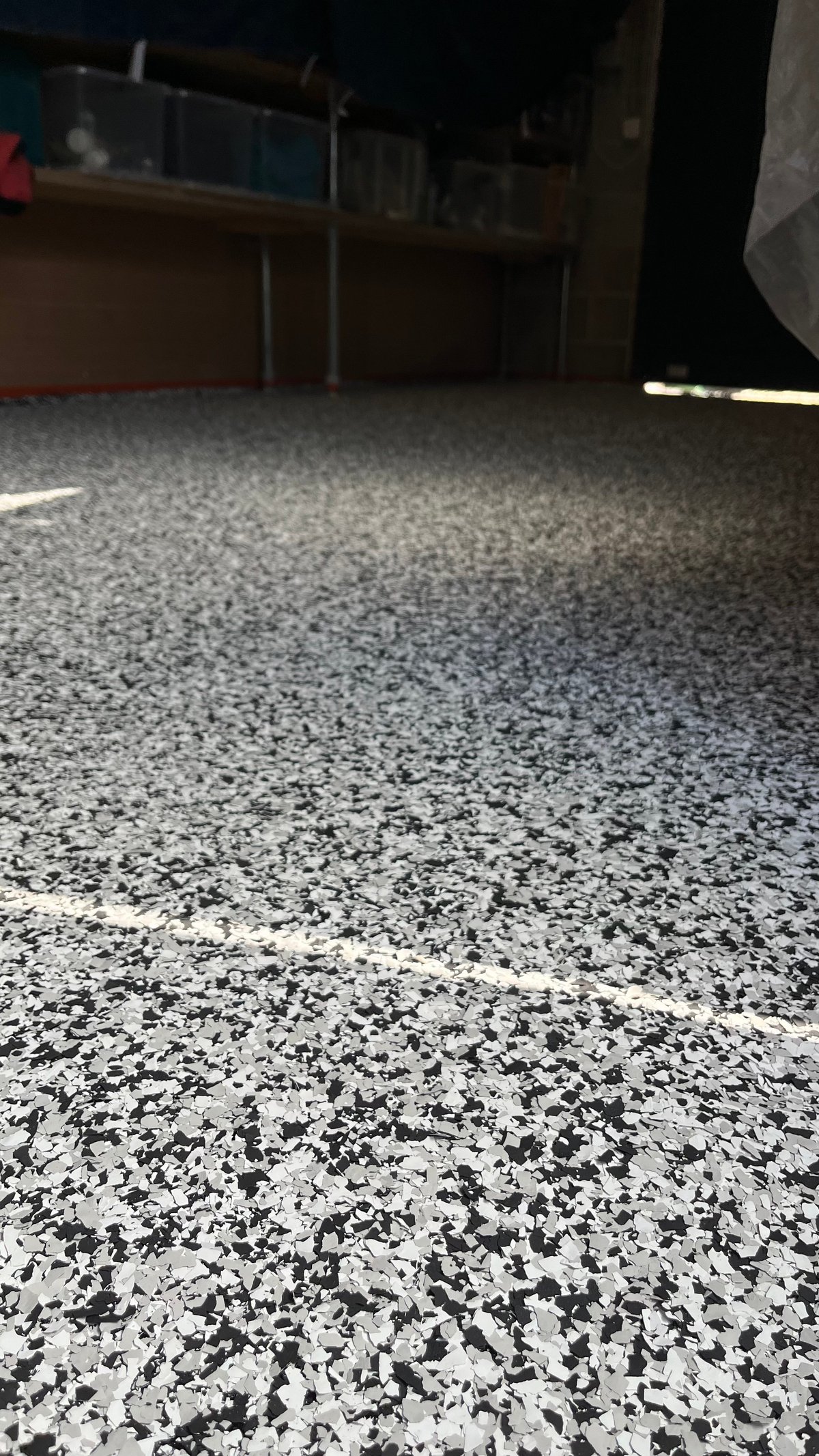 Low angle view of a speckled gray and white garage floor with workbench and storage shelving in background