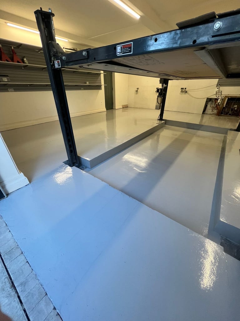 Empty garage interior with hydraulic car lift and white epoxy flooring