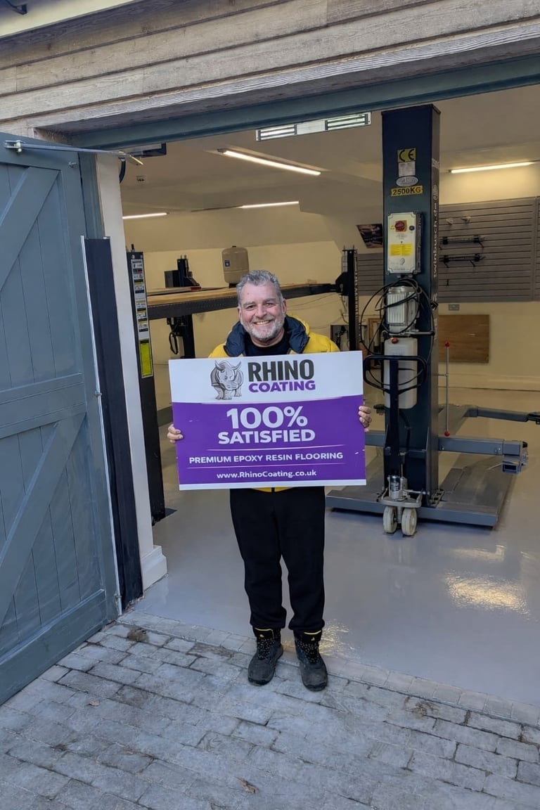 Man holding Rhino Coating satisfaction sign in a garage workshop with epoxy flooring