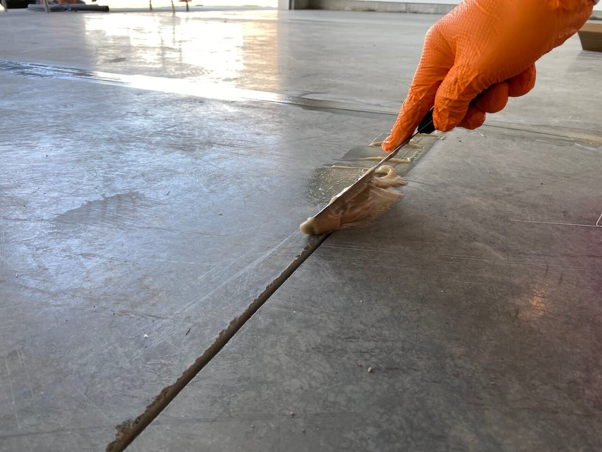 Hand in orange glove applying sealant or filler to a concrete floor seam with a brush