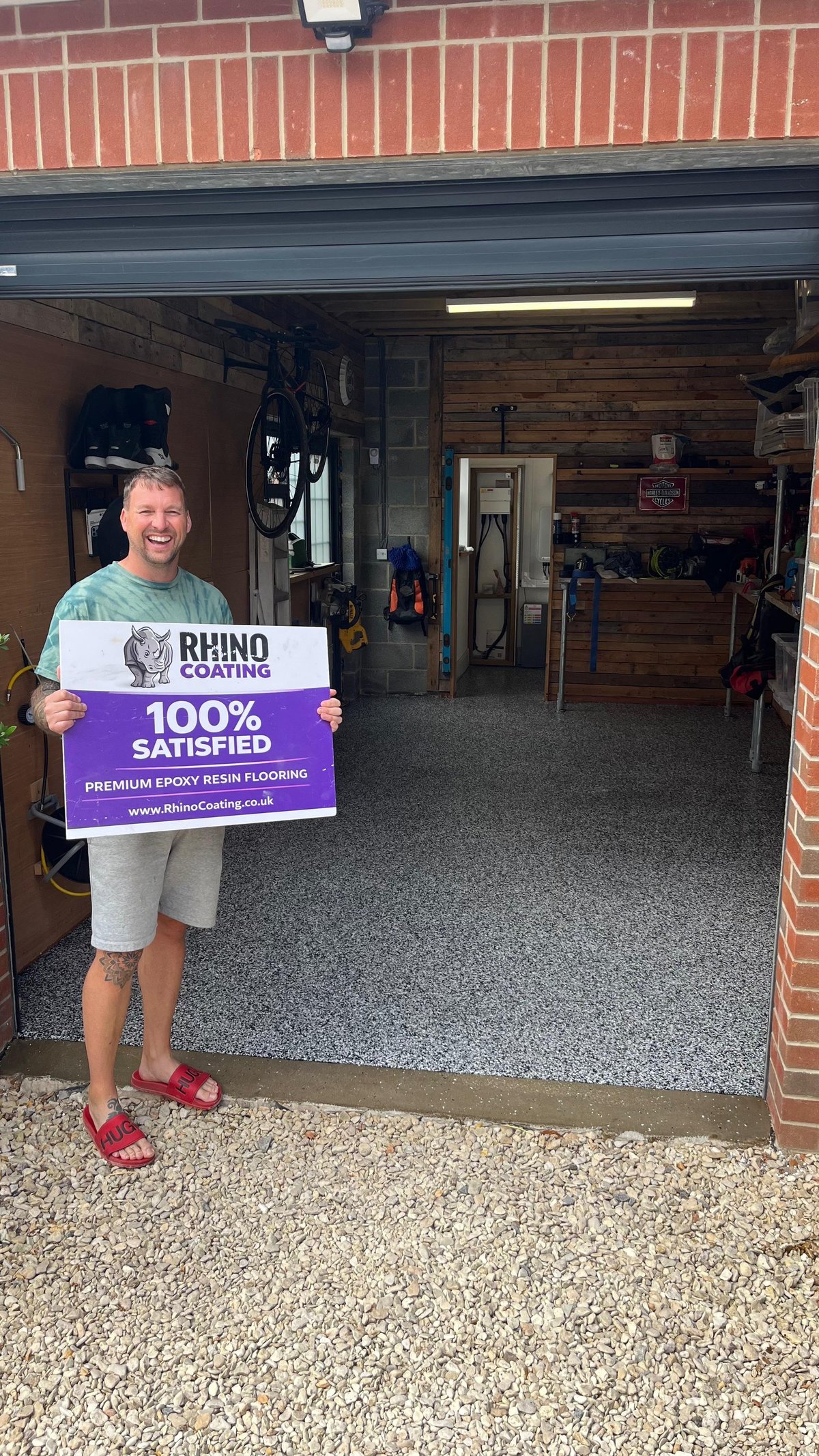 Man holding Rhino Coating 100% Satisfied sign in garage with premium epoxy resin flooring