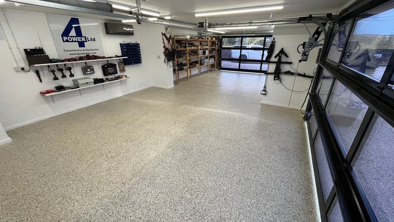 Empty spacious workshop or garage with control panels on left wall, storage shelves in center, large windows on right, and fluorescent ceiling lights